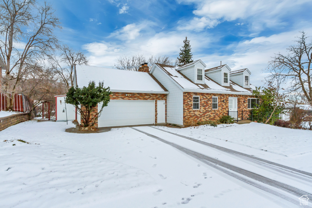Snow covered property featuring a chimney, a garage, and brick siding