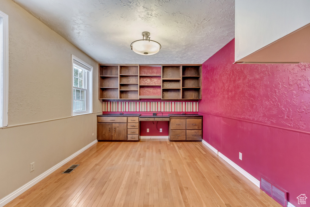 Unfurnished office with a textured ceiling, visible vents, light wood-type flooring, and built in study area