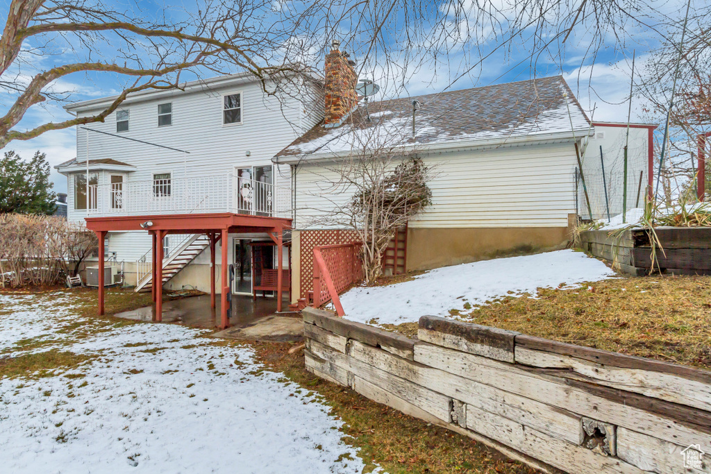 Snow covered back of property featuring stairway, roof with shingles, a chimney, a wooden deck, and central AC unit