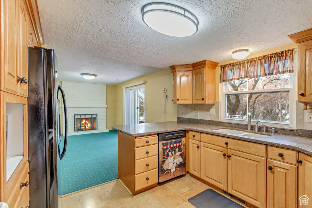 Kitchen featuring a brick fireplace, a peninsula, dark countertops, a sink, and freestanding refrigerator
