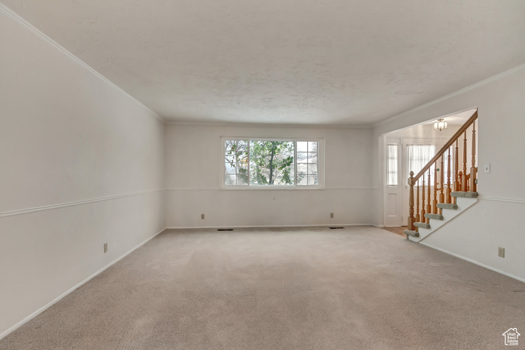 Empty room featuring light carpet, a notable chandelier, crown molding, and stairway