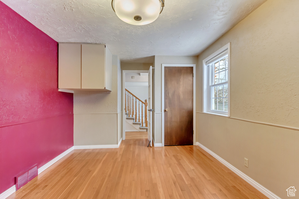 Unfurnished room with a textured wall, stairs, visible vents, and light wood-style floors