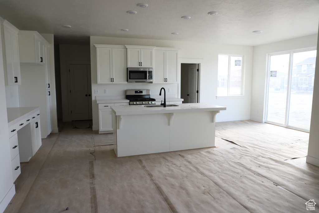 Kitchen with light countertops, a center island with sink, a sink, white cabinets, and appliances with stainless steel finishes