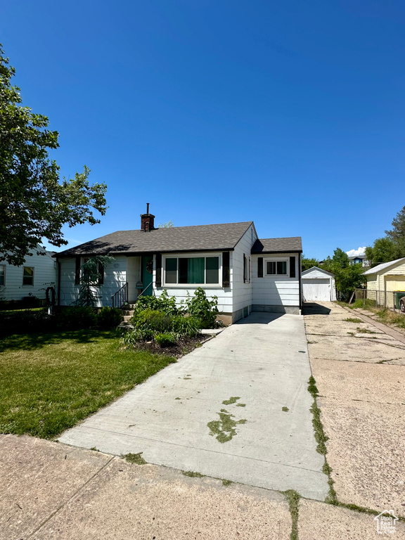 Ranch-style home featuring a front lawn, a chimney, a garage, a shingled roof, and an outbuilding