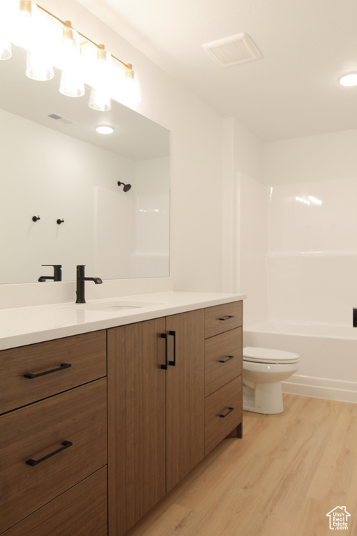 Full bathroom with toilet, vanity, visible vents, and wood finished floors