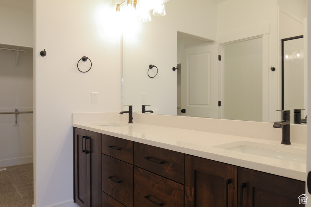 Bathroom featuring an inviting chandelier, double vanity, a sink, and a walk in closet