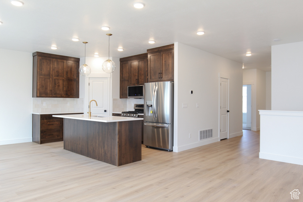 Kitchen featuring light wood finished floors, visible vents, dark brown cabinetry, backsplash, and stainless steel appliances