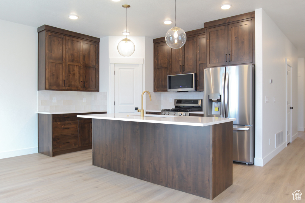 Kitchen with baseboards, a sink, backsplash, light wood-style floors, and stainless steel appliances