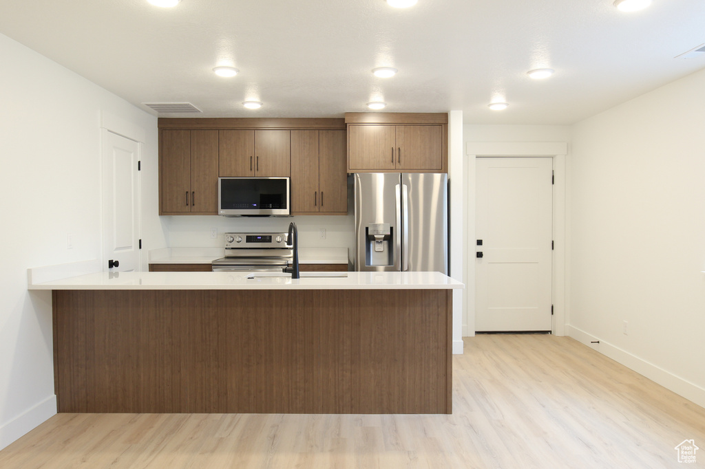Kitchen with light wood-style flooring, baseboards, light countertops, and appliances with stainless steel finishes