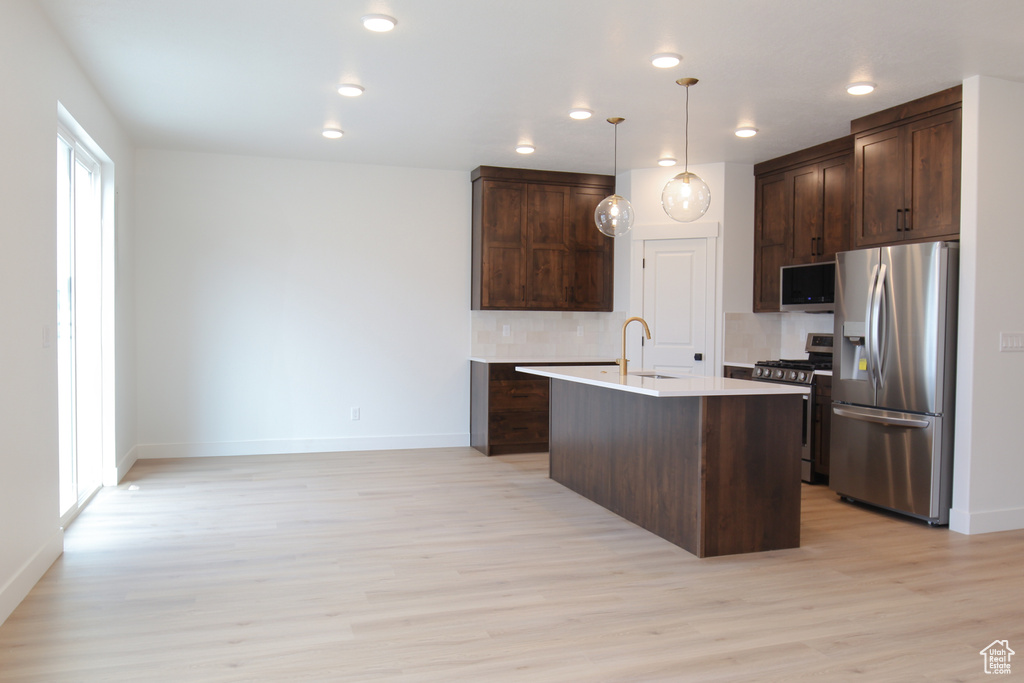 Kitchen featuring stainless steel appliances, dark brown cabinetry, light wood-style flooring, light countertops, and baseboards