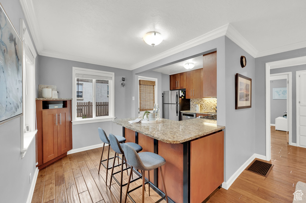 Kitchen featuring visible vents, ornamental molding, appliances with stainless steel finishes, light wood-style floors, and a breakfast bar area