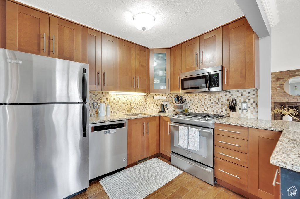 Kitchen with light stone countertops, a sink, light wood-style floors, and appliances with stainless steel finishes
