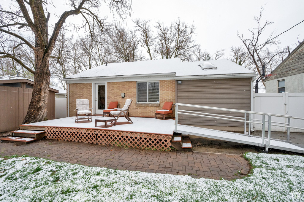 Rear view of property featuring a wooden deck, fence, brick siding, and a patio