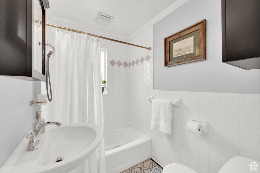 Bathroom with crown molding, toilet, a sink, visible vents, and tile walls
