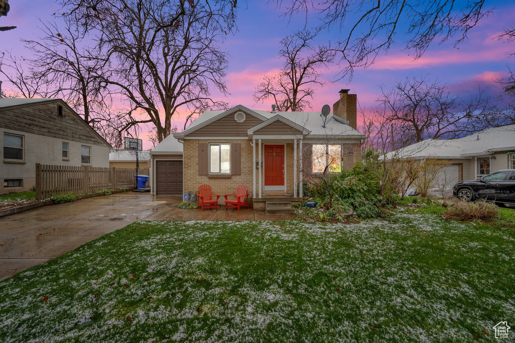 Bungalow with concrete driveway, fence, a front lawn, brick siding, and a chimney