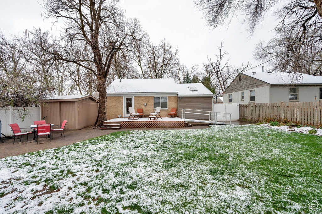Snow covered property with a fenced backyard, a lawn, a deck, and an outdoor structure