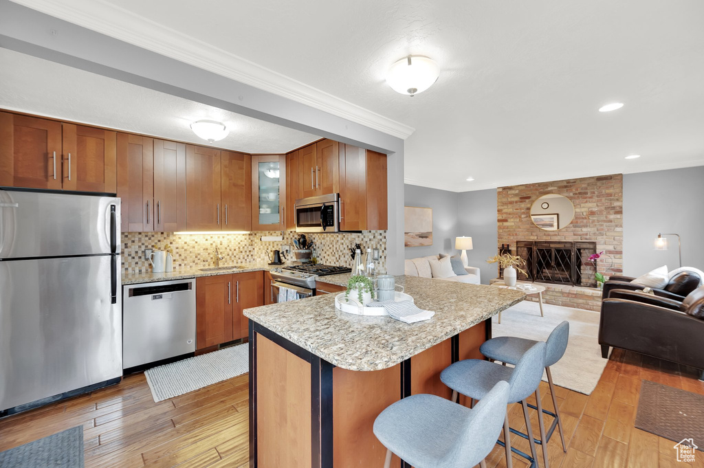 Kitchen with light wood-style flooring, tasteful backsplash, appliances with stainless steel finishes, and brown cabinets