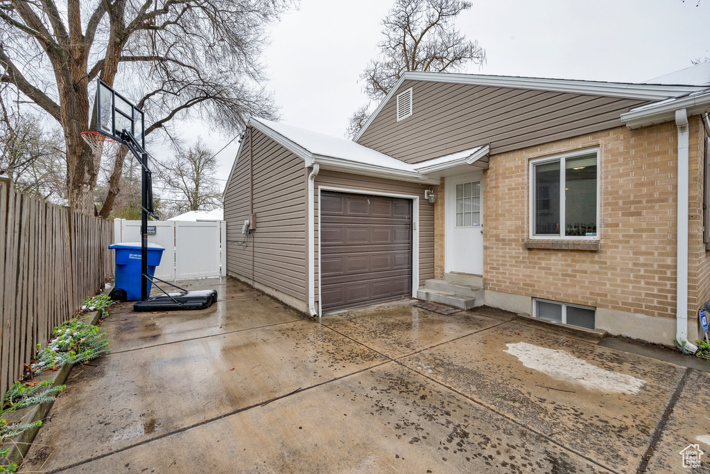 Exterior space featuring fence, entry steps, a garage, concrete driveway, and brick siding