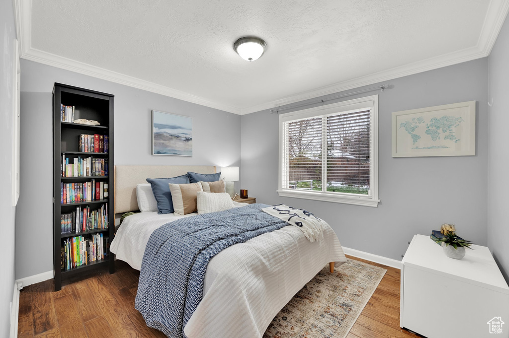 Bedroom featuring ornamental molding, a textured ceiling, baseboards, and wood finished floors