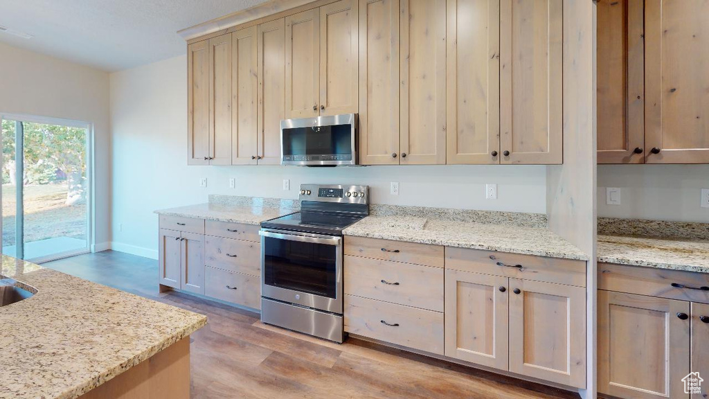 Kitchen featuring light brown cabinets, light stone countertops, stainless steel appliances, and light wood-type flooring