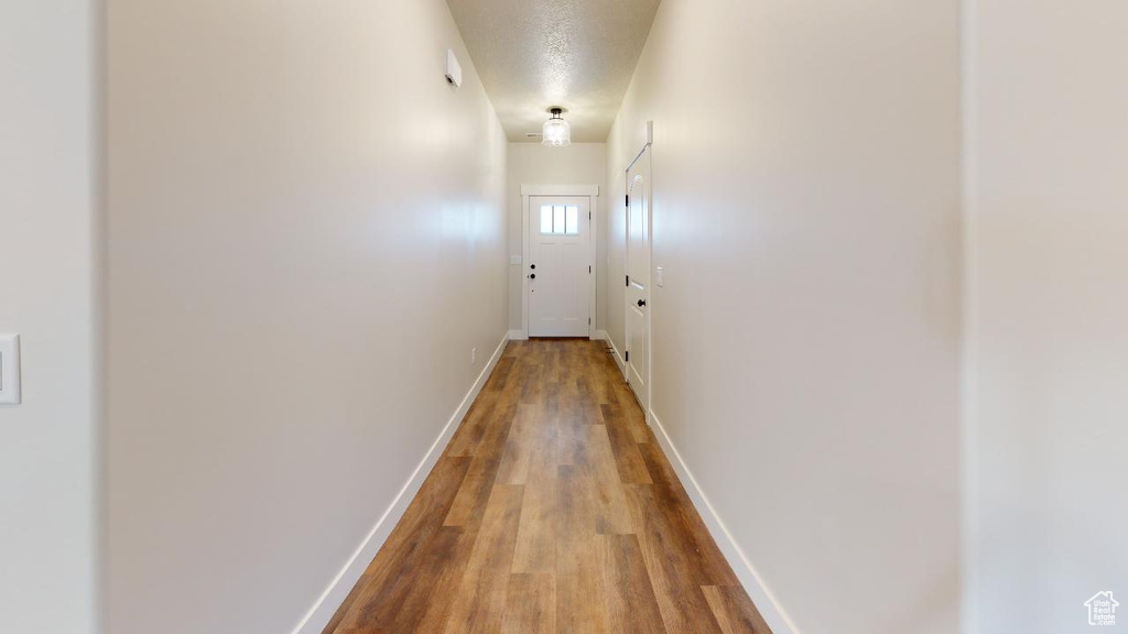 Hall featuring baseboards, wood finished floors, and a textured ceiling