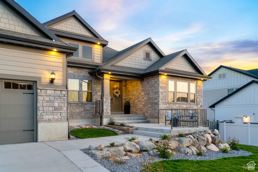 View of front of property featuring stone siding, a shingled roof, driveway, and a garage