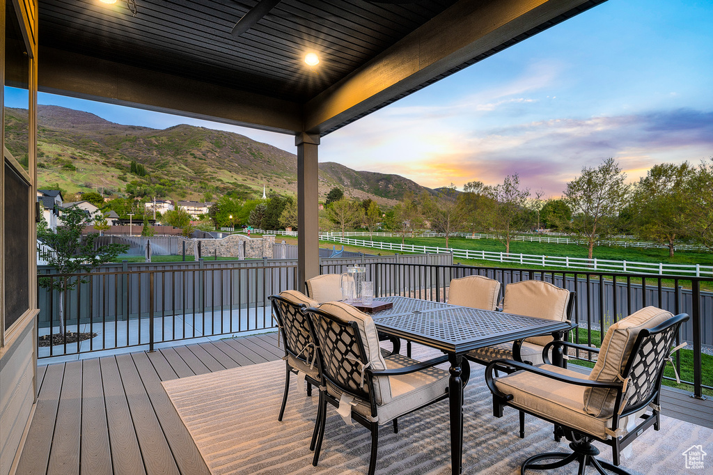 Deck at dusk featuring fence, outdoor dining space, and a mountain view