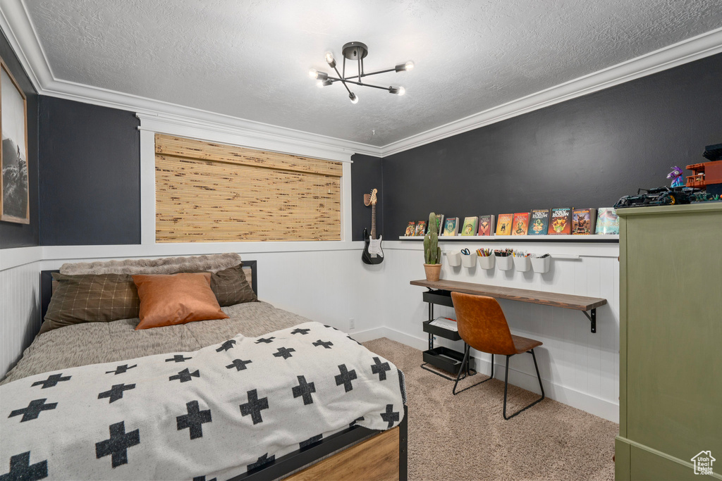 Bedroom with a wainscoted wall, a textured ceiling, a chandelier, carpet, and ornamental molding