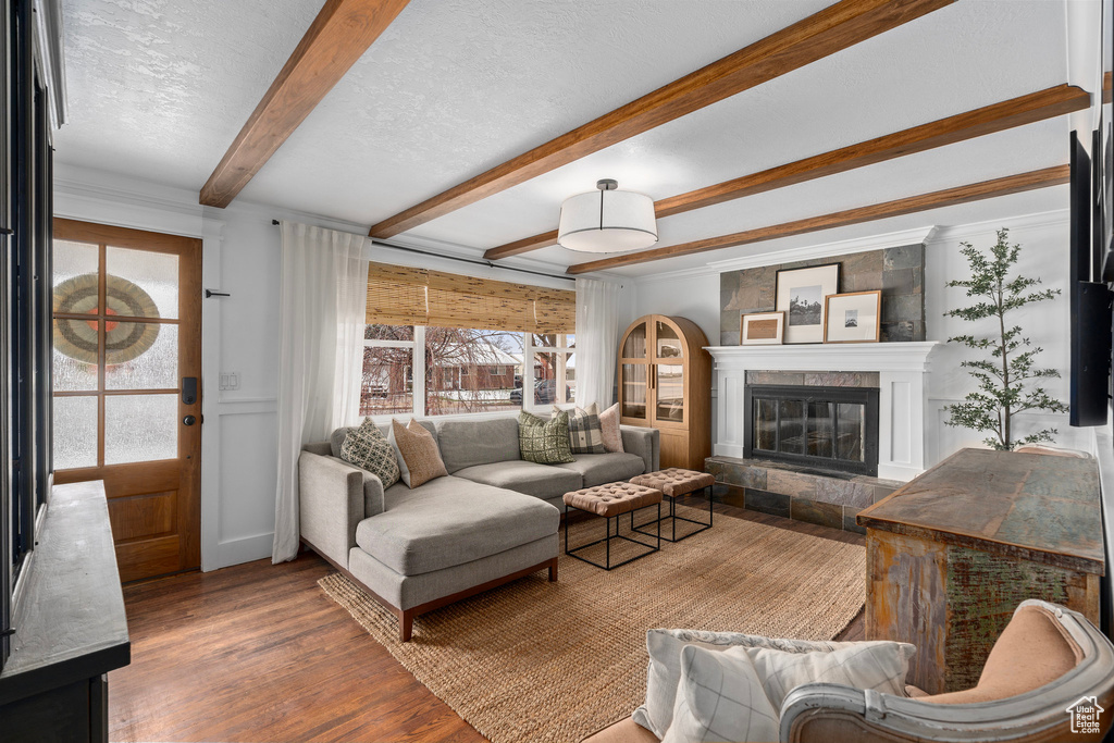 Living room featuring a textured ceiling, wood finished floors, a tiled fireplace, and beam ceiling