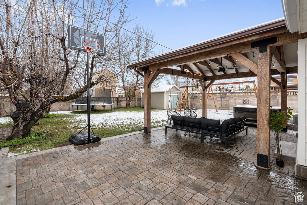 View of patio with a trampoline, a fenced backyard, a hot tub, an outbuilding, and a shed