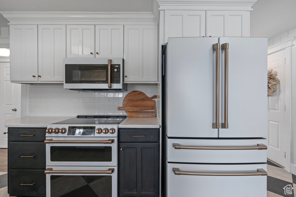 Kitchen featuring high end appliances, light countertops, white cabinetry, and backsplash
