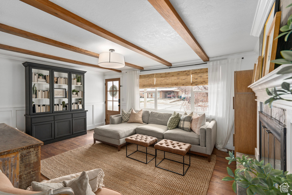 Living area featuring a decorative wall, wood finished floors, beam ceiling, and a textured ceiling