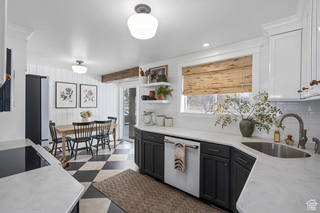 Kitchen featuring dark floors, dishwasher, tasteful backsplash, a sink, and freestanding refrigerator