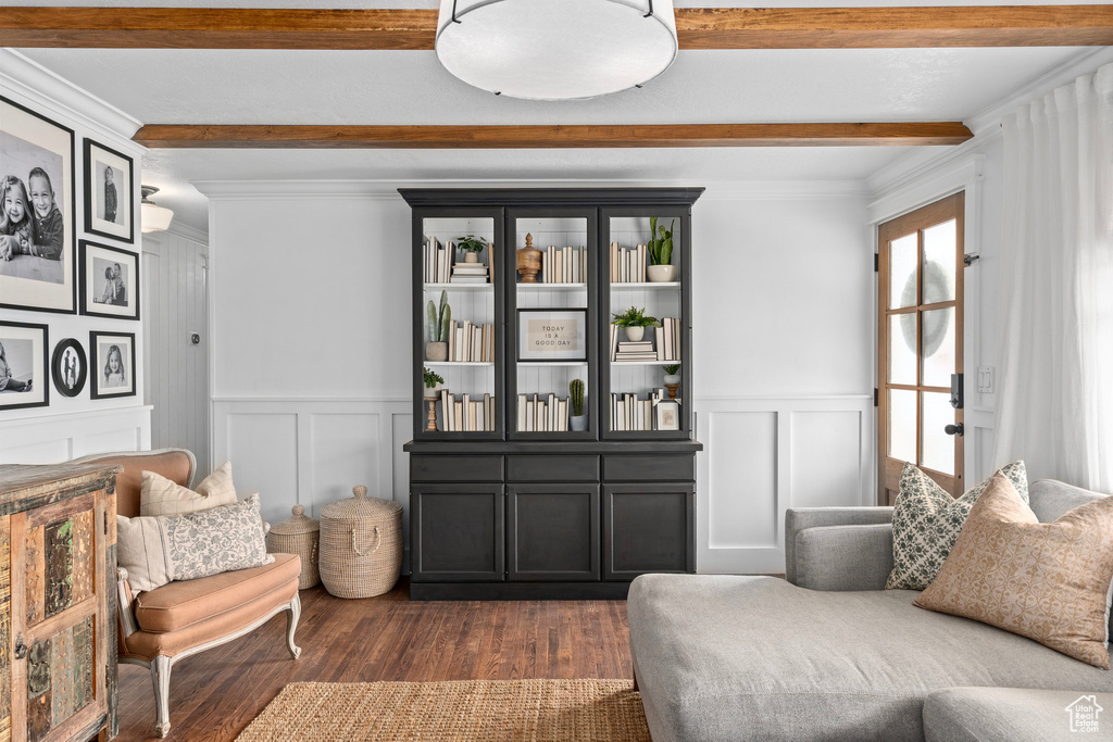 Sitting room featuring a decorative wall, dark wood-style flooring, beam ceiling, and crown molding