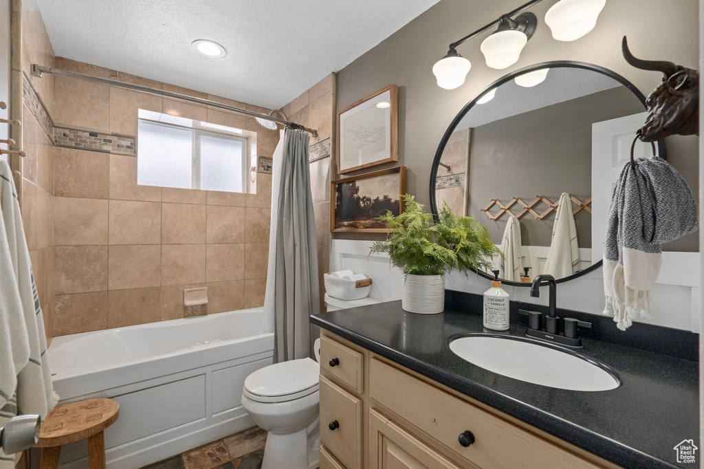 Full bath featuring toilet, shower / bath combo with shower curtain, a textured ceiling, and vanity