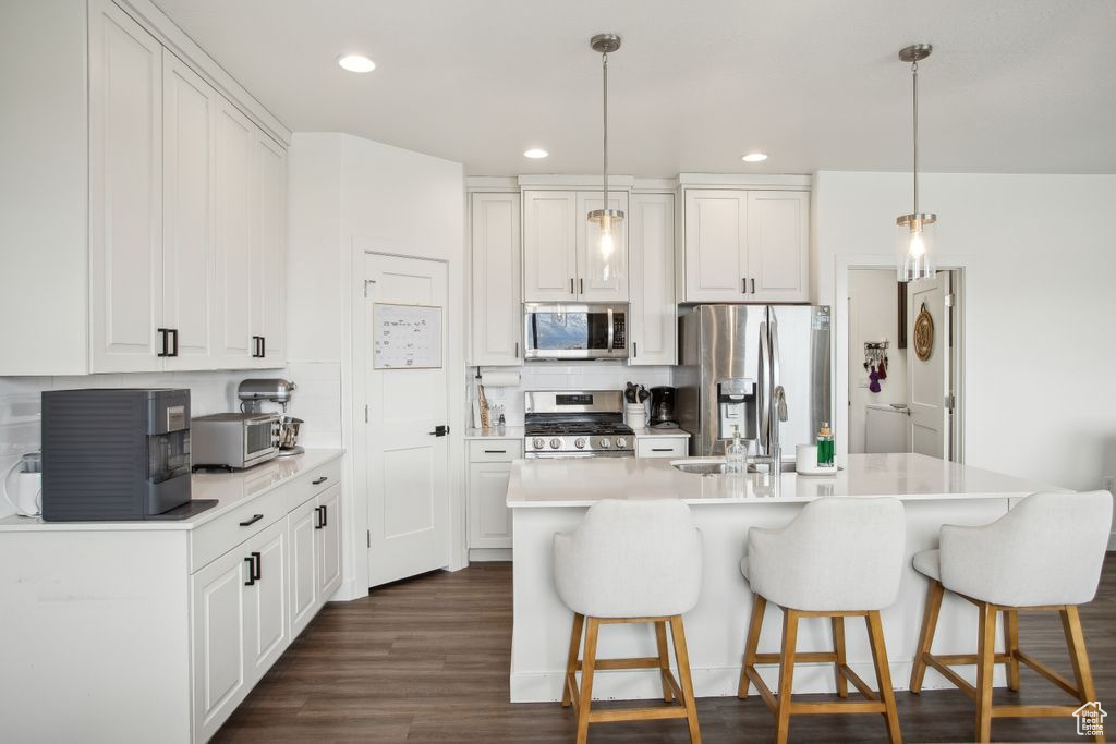 Kitchen featuring white cabinets, stainless steel appliances, a kitchen breakfast bar, and tasteful backsplash