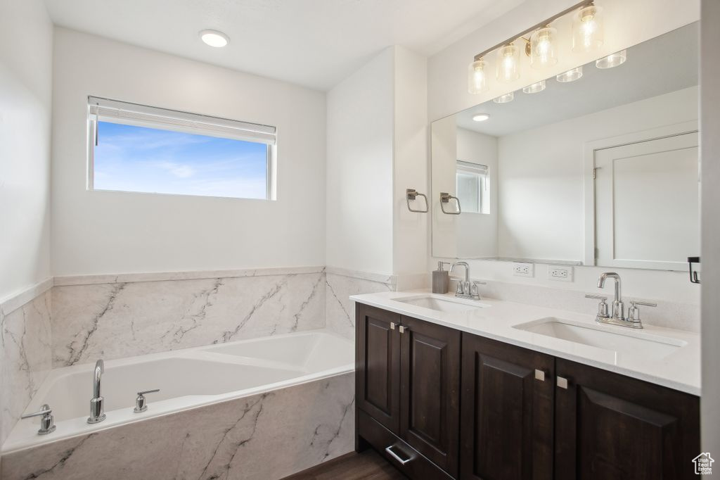 Full bath with double vanity, a sink, and a garden tub