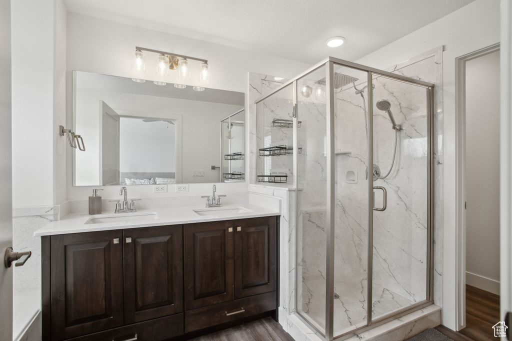 Bathroom with a marble finish shower, double vanity, a sink, and wood finished floors