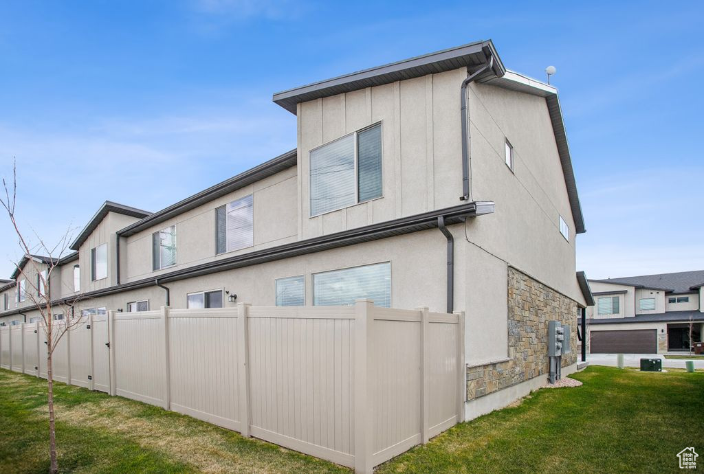 Rear view of property with fence, a lawn, stucco siding, and stone siding