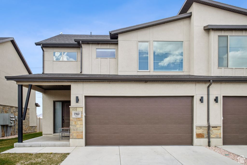View of front of house featuring driveway, stone siding, roof with shingles, stucco siding, and an attached garage