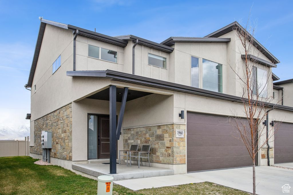 View of front of house featuring stone siding, stucco siding, a patio area, and an attached garage