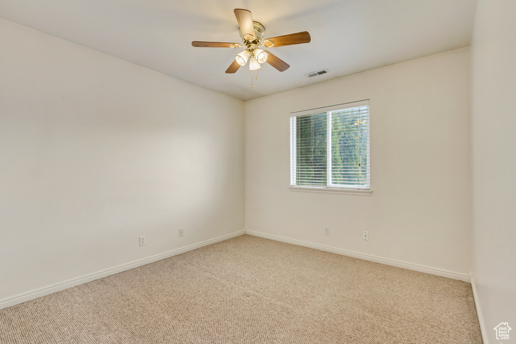 Carpeted empty room with baseboards, visible vents, and ceiling fan
