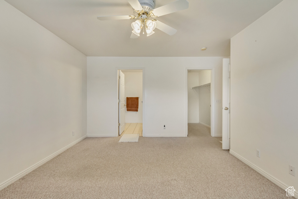 Unfurnished bedroom featuring a spacious closet, light carpet, connected bathroom, and baseboards