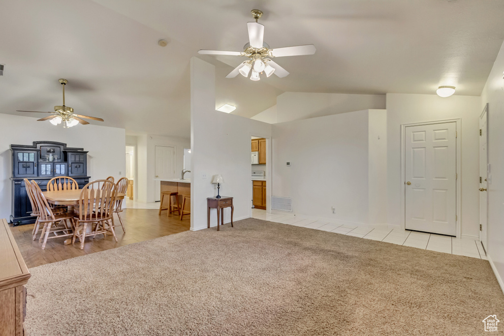 Living room featuring light colored carpet, lofted ceiling, visible vents, and ceiling fan