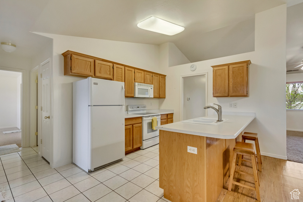Kitchen with a kitchen breakfast bar, light countertops, white appliances, a sink, and a peninsula