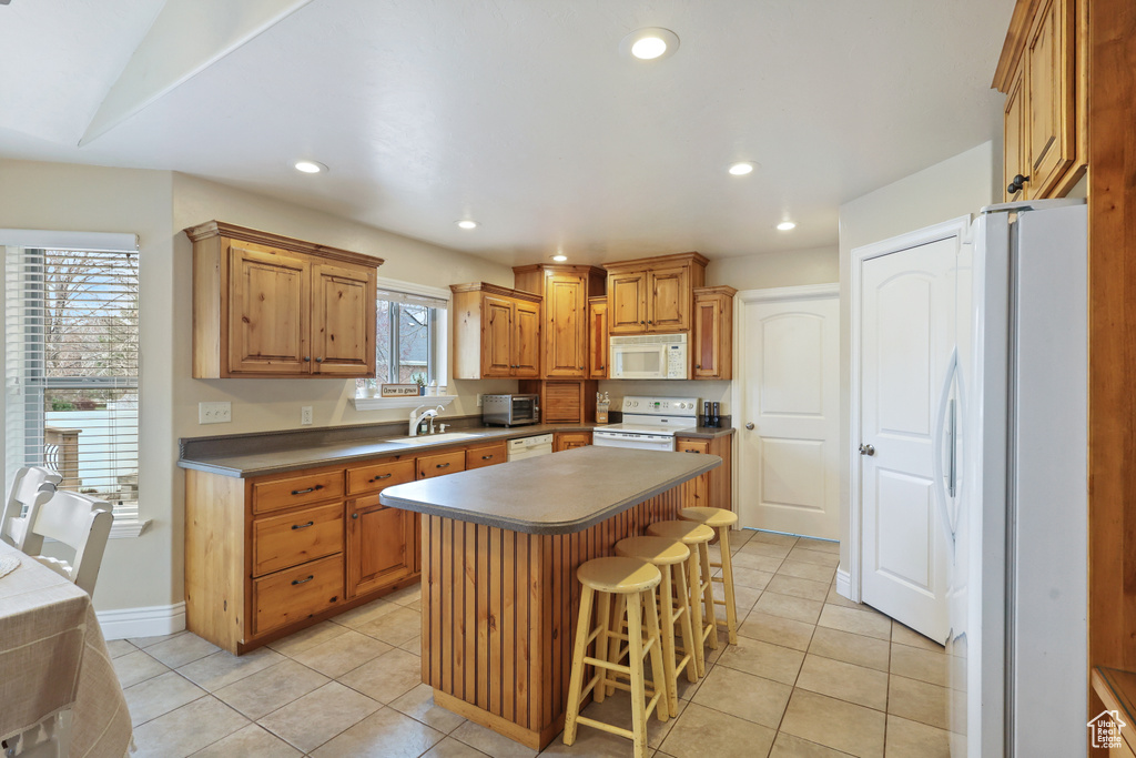 Kitchen with recessed lighting, white appliances, a kitchen island, a sink, and light tile patterned flooring
