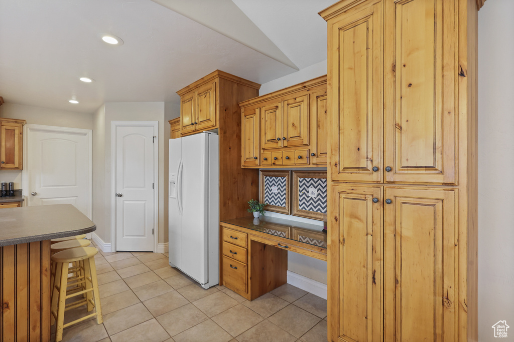Kitchen featuring built in desk, a breakfast bar area, light tile patterned floors, white refrigerator with ice dispenser, and dark countertops