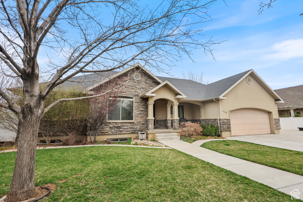 View of front facade with stone siding, driveway, an attached garage, a front yard, and stucco siding