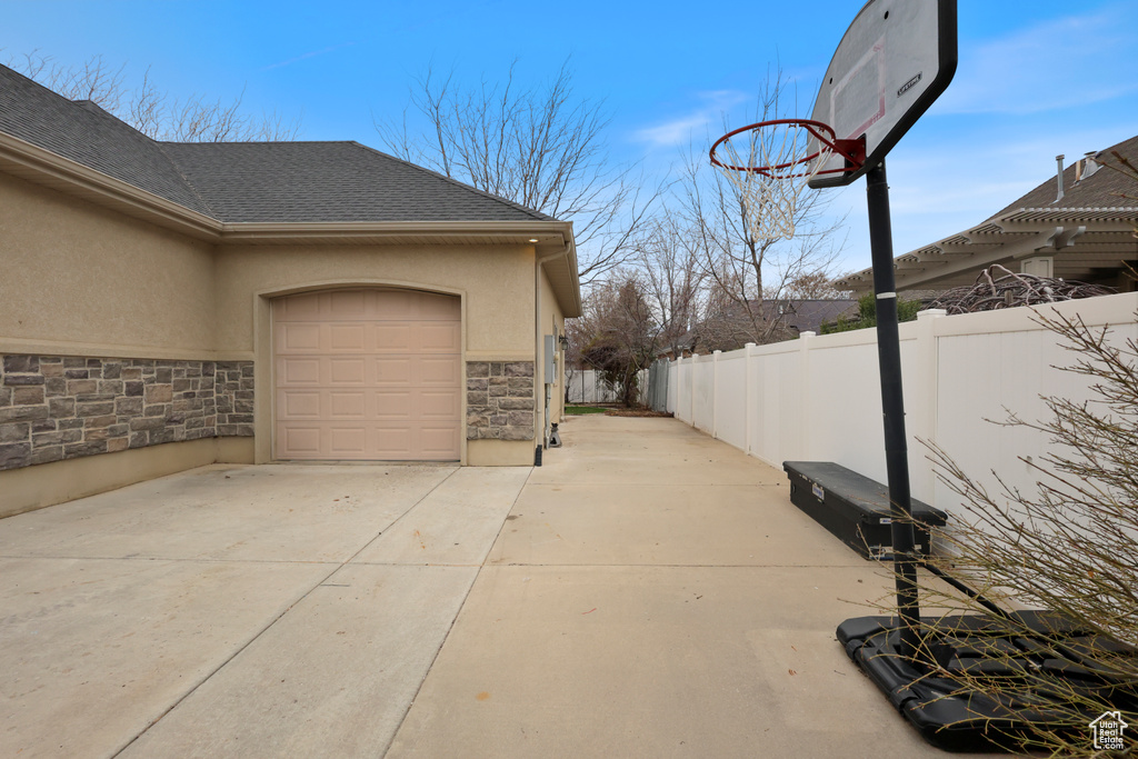 View of side of home with driveway, stone siding, stucco siding, fence, and an attached garage