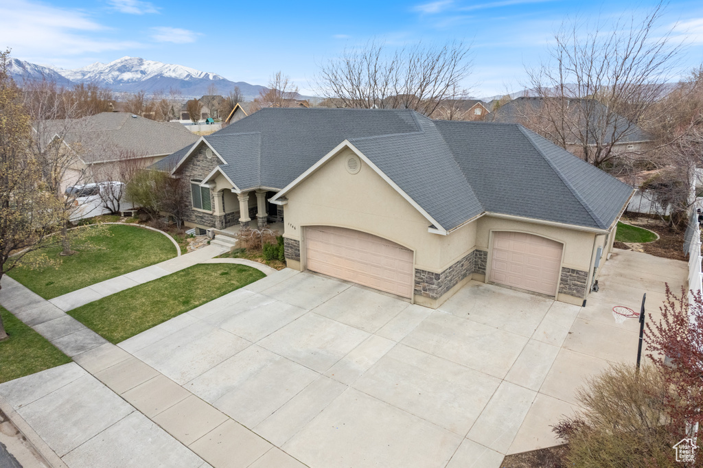 View of front of property with stucco siding, an attached garage, stone siding, a mountain view, and a front lawn